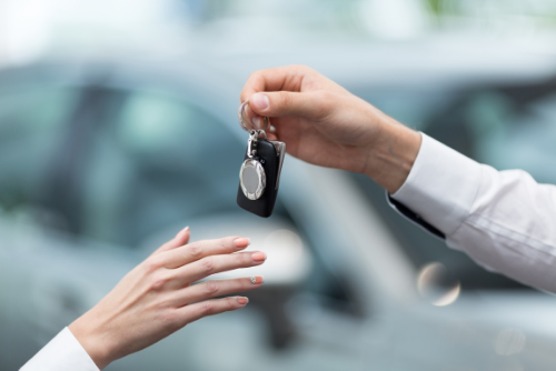 A new car buyer's hand reaches out to accept set of keys from hand of dealership employee